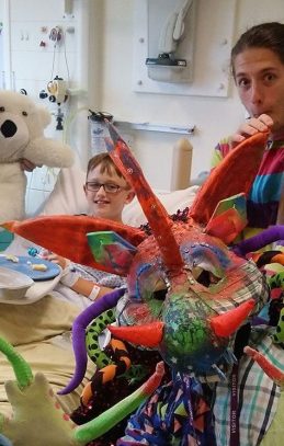 2Faced Dance's colourful dragon and two other performers interact with boy in bed