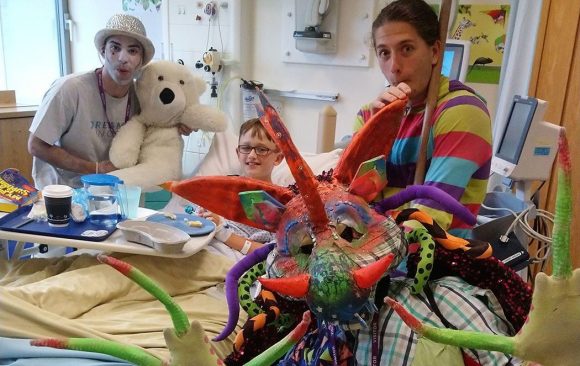 2Faced Dance's colourful dragon and two other performers interact with boy in bed