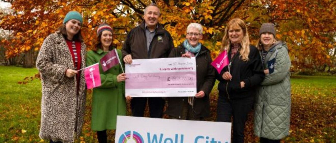 Team from Well-City pose with a large cheque in front of autumn trees