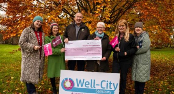 Team from Well-City pose with a large cheque in front of autumn trees