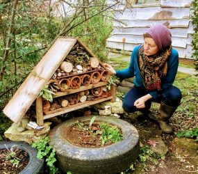 Hannah looks at her wooden hut shape filled with logs with holes drilled in, flower pots with twigs, leaves and pine cones to hide in