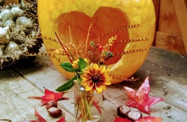 pumpkin with heart shape carved out, conkers, leaves and a posy of flowers and stems in a jam jar