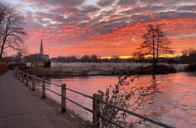 photo of pink sunrise behind silhouette of Salisbury Cathedral viewed across water meadows